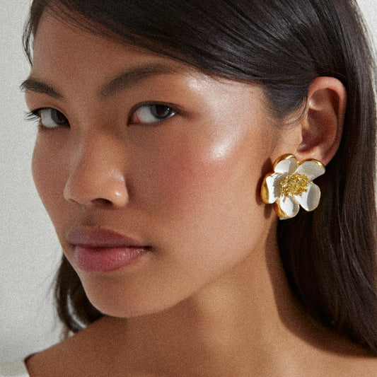 Woman wearing a white and gold floral earring against a neutral background