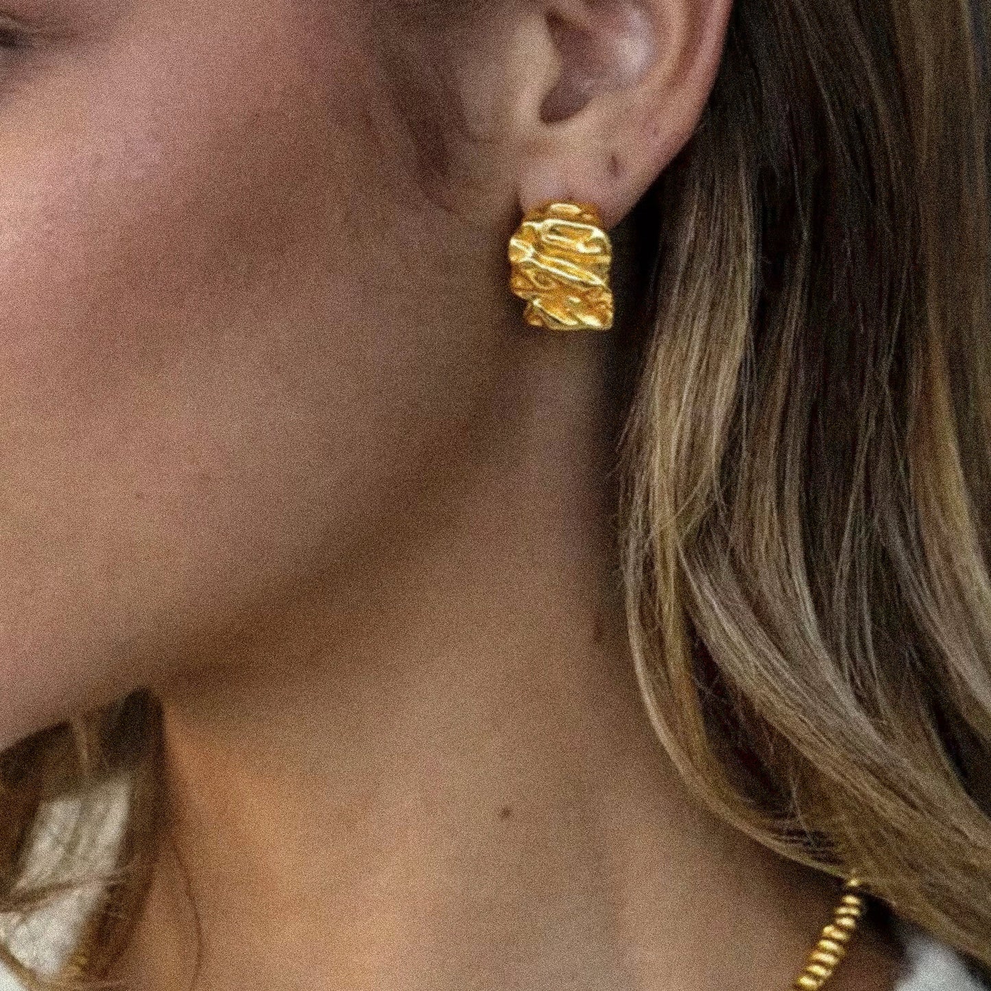 Close-up of a person wearing gold earrings with a blurred background
