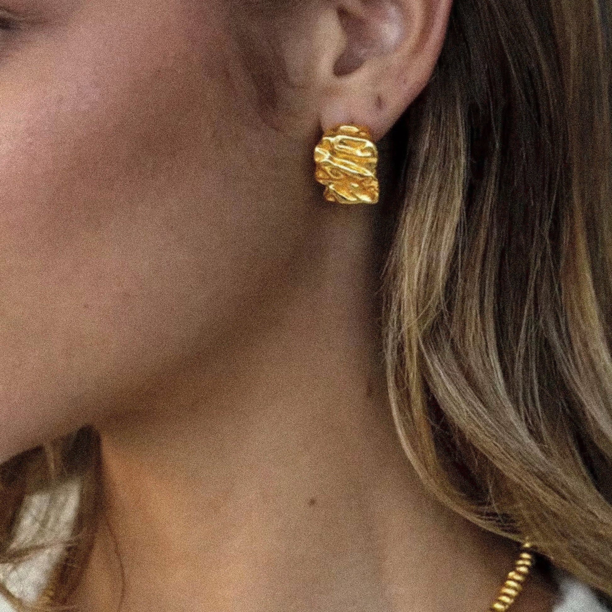 Close-up of a person wearing gold earrings with a blurred background