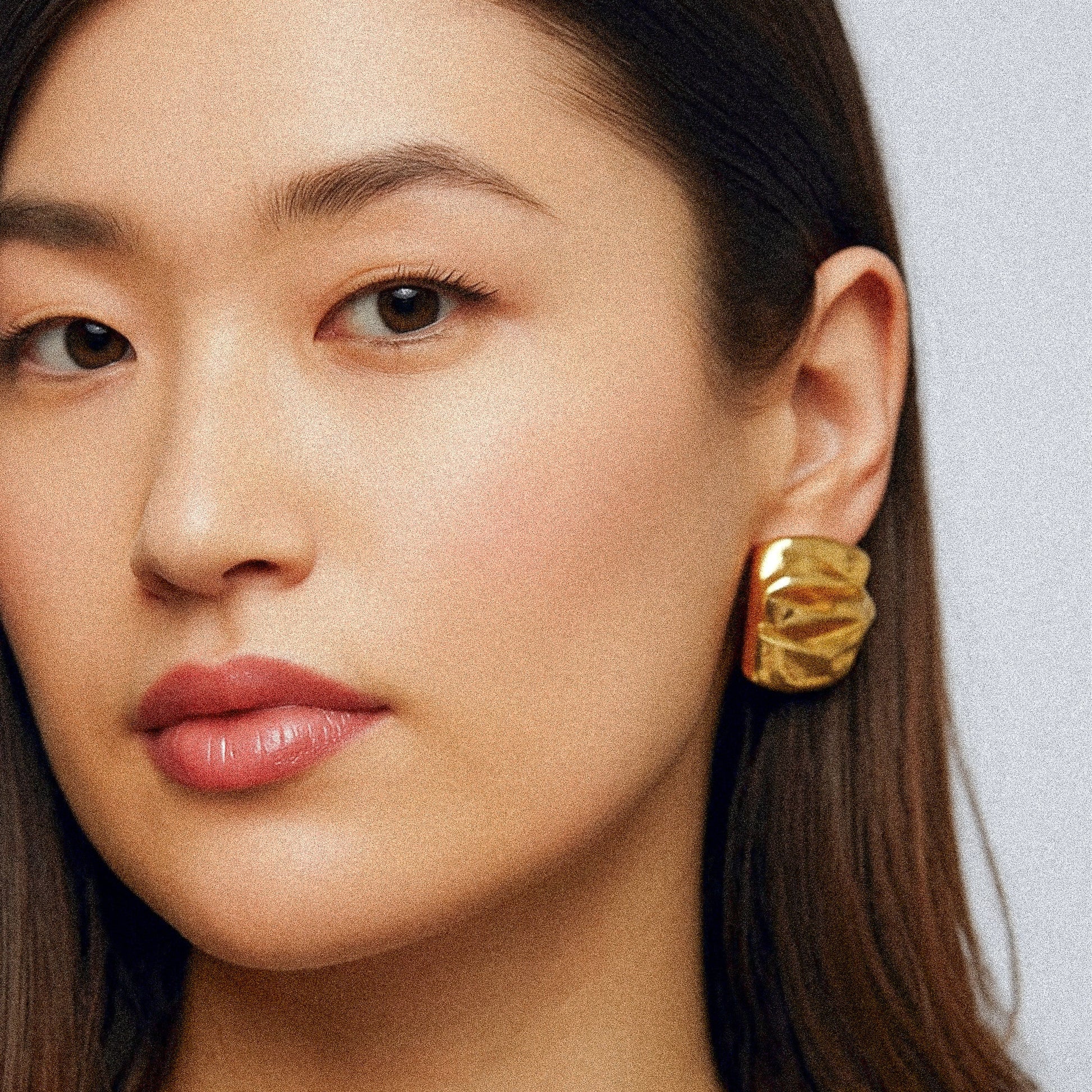 Close-up of a woman wearing gold earrings with a plain background