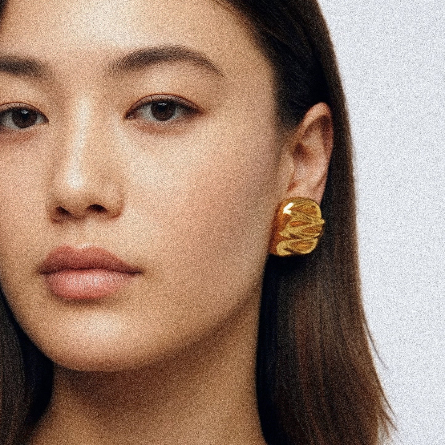 Close-up of a woman wearing a gold earring against a light background