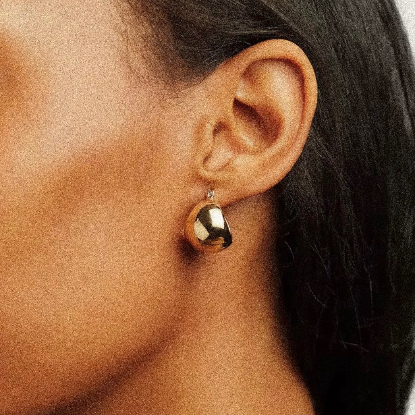 Gold earring worn by a woman with dark skin and dark hair.