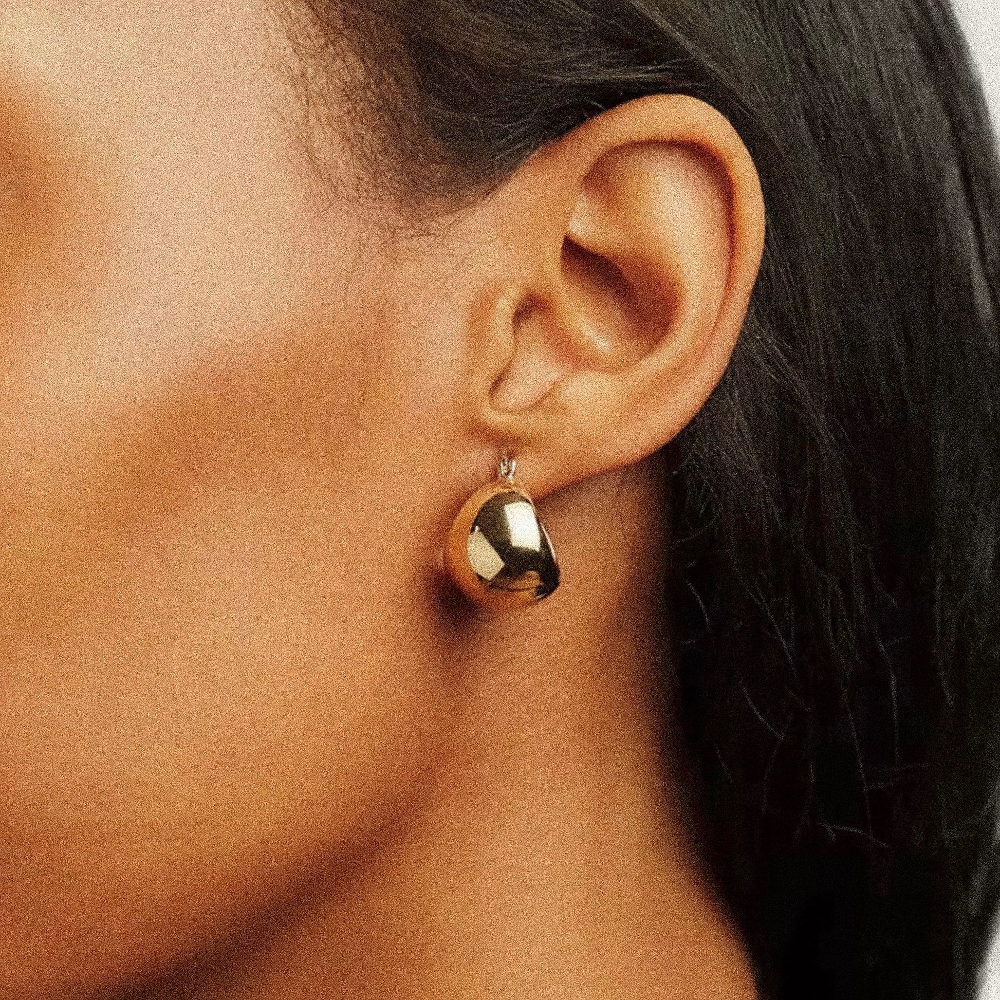 Gold earring worn by a woman with dark skin and dark hair.