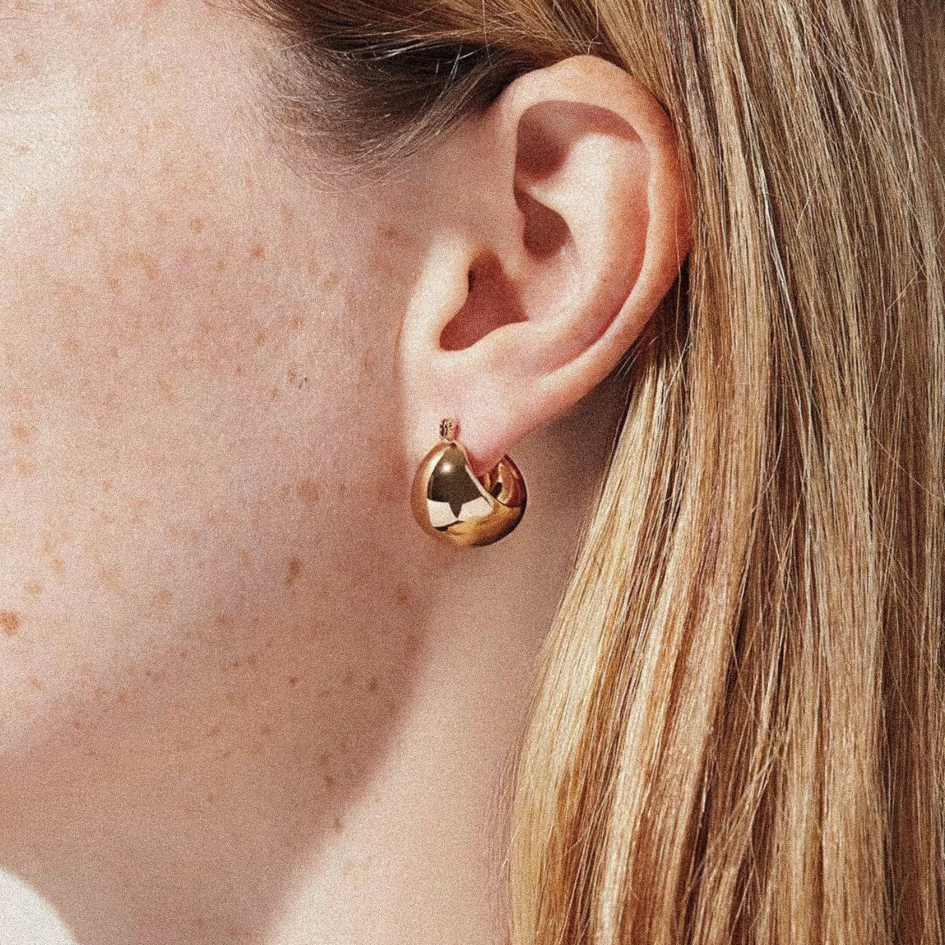 Gold hoop earring worn by a woman with fair skin and blonde hair.
