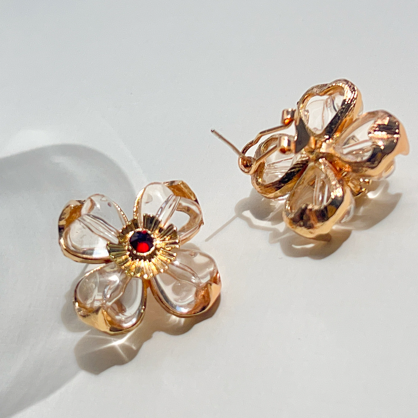 Gold flower-shaped earrings with a red gemstone on a light background
