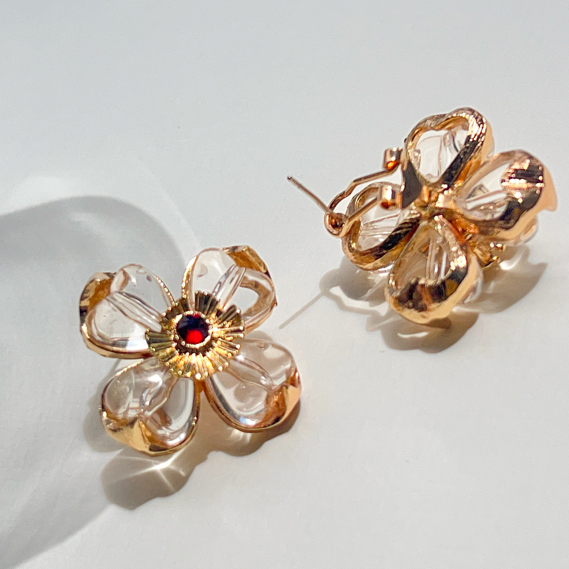 Gold flower-shaped earrings with a red gemstone on a light background