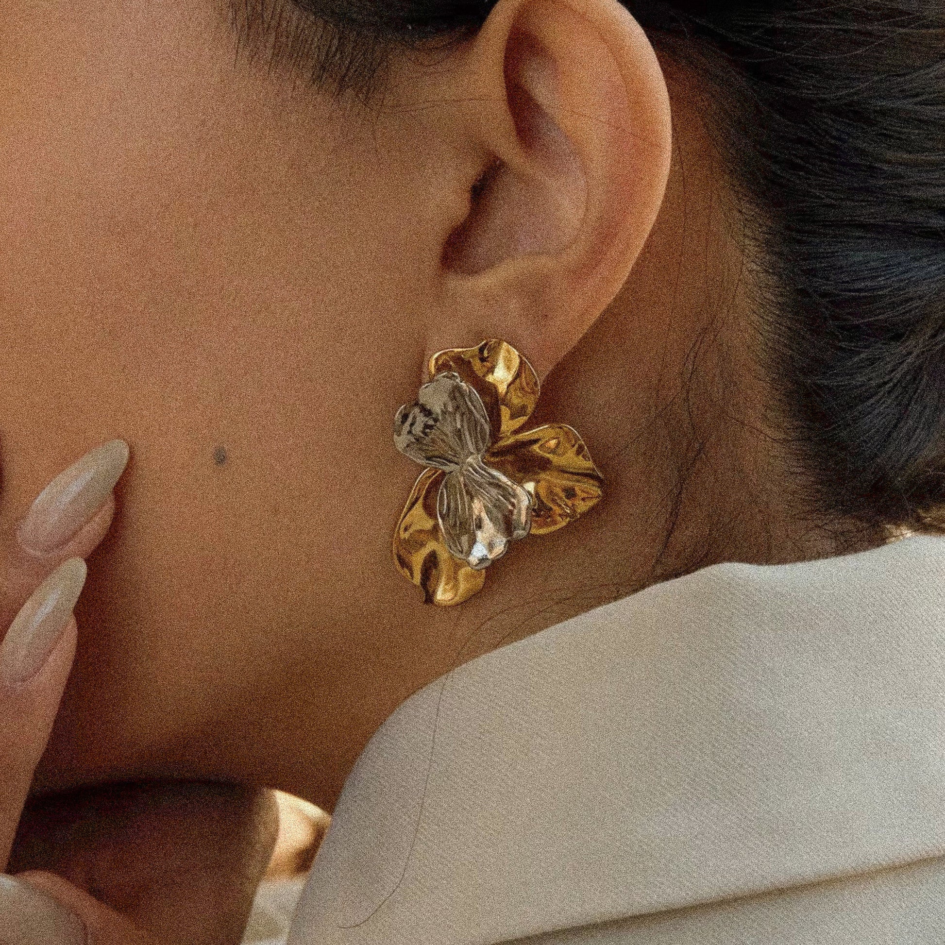 Close-up of a person wearing a gold bow-shaped earring.