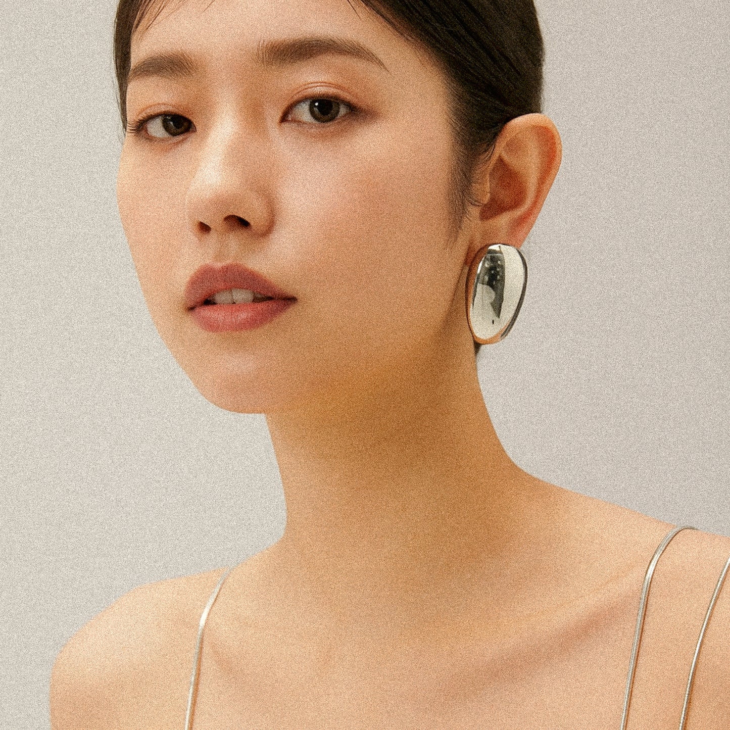 Close-up of a woman wearing silver oval earrings against a neutral background