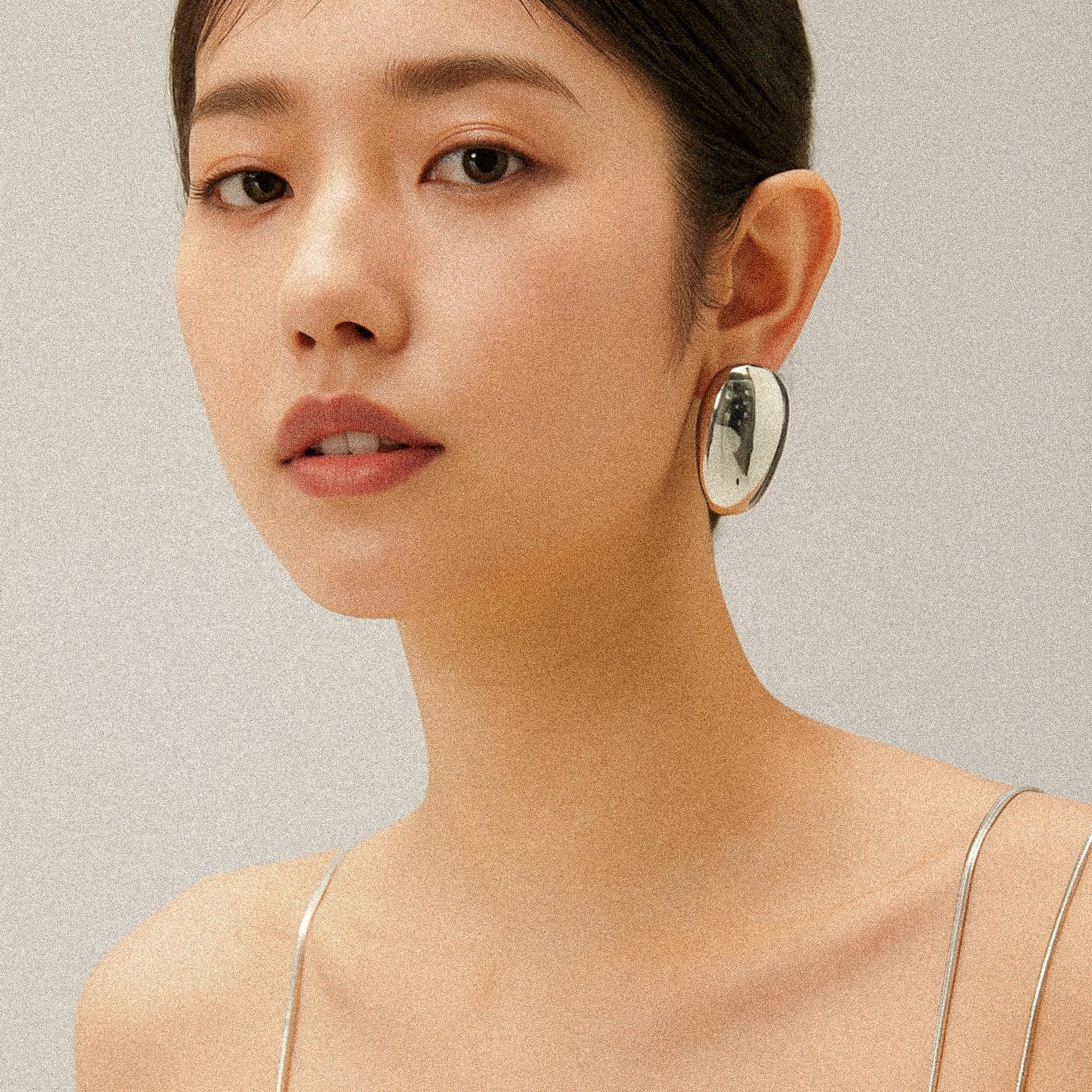 Close-up of a woman wearing silver oval earrings against a neutral background