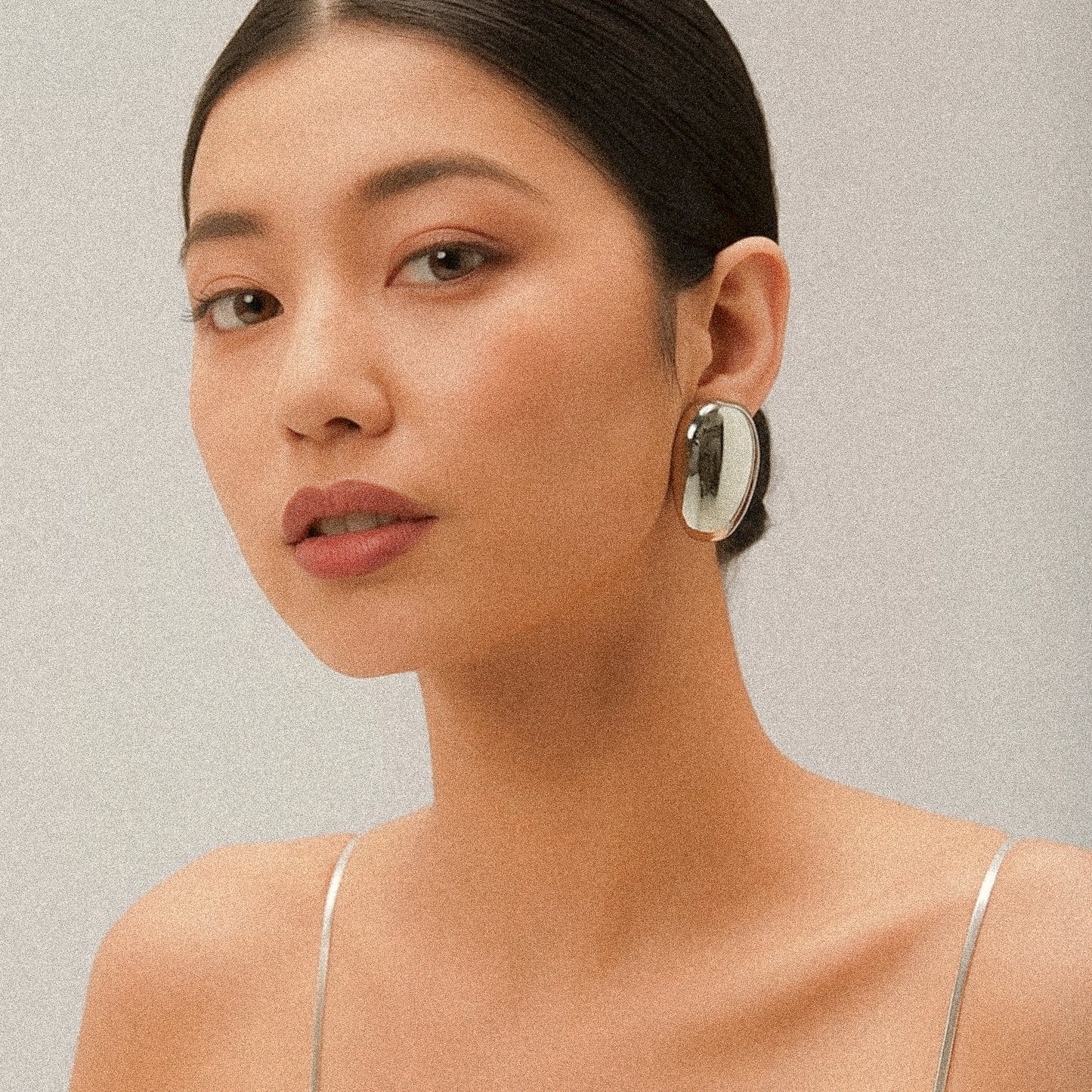 Woman wearing a silver oval earring against a neutral background