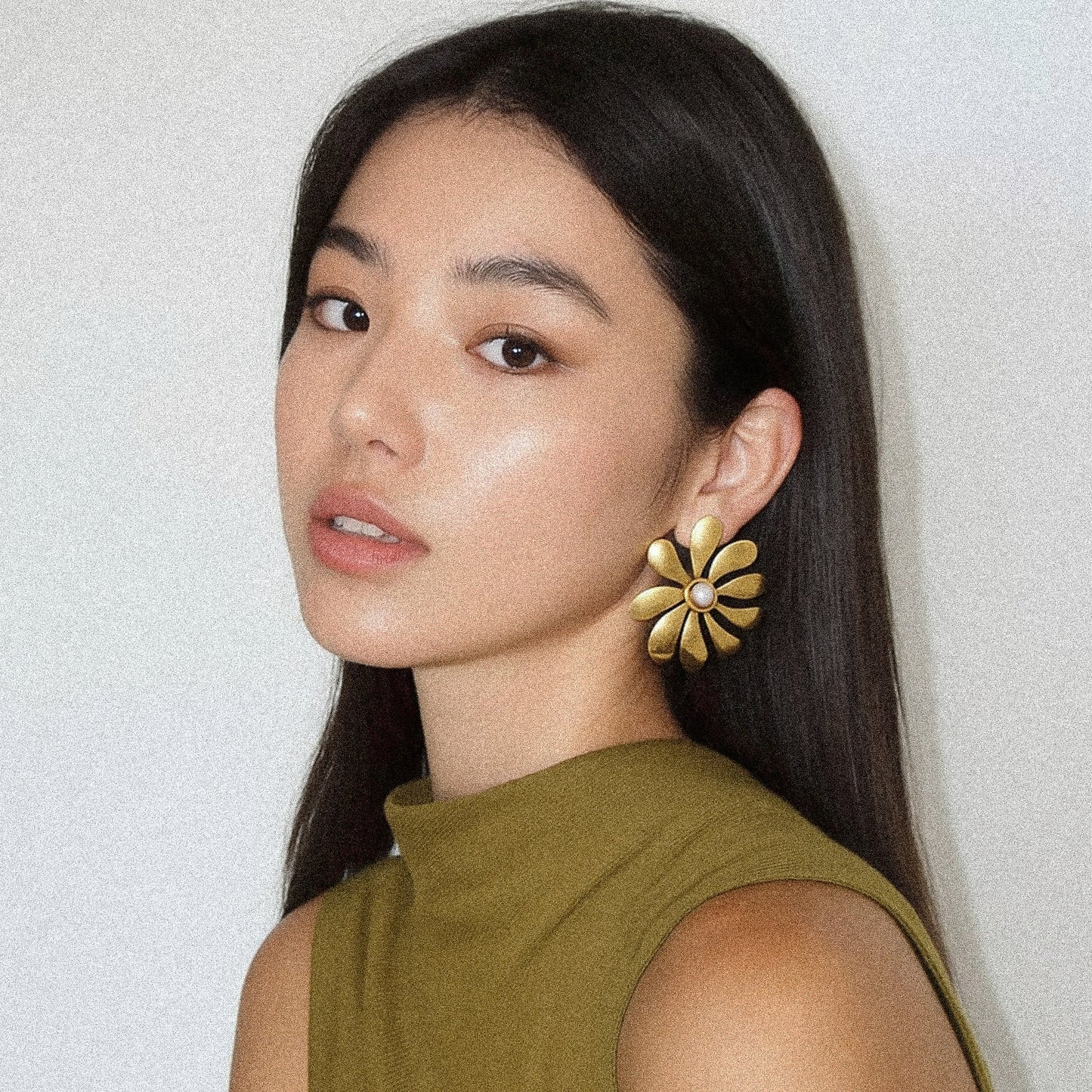 Woman wearing gold floral earrings against a light background
