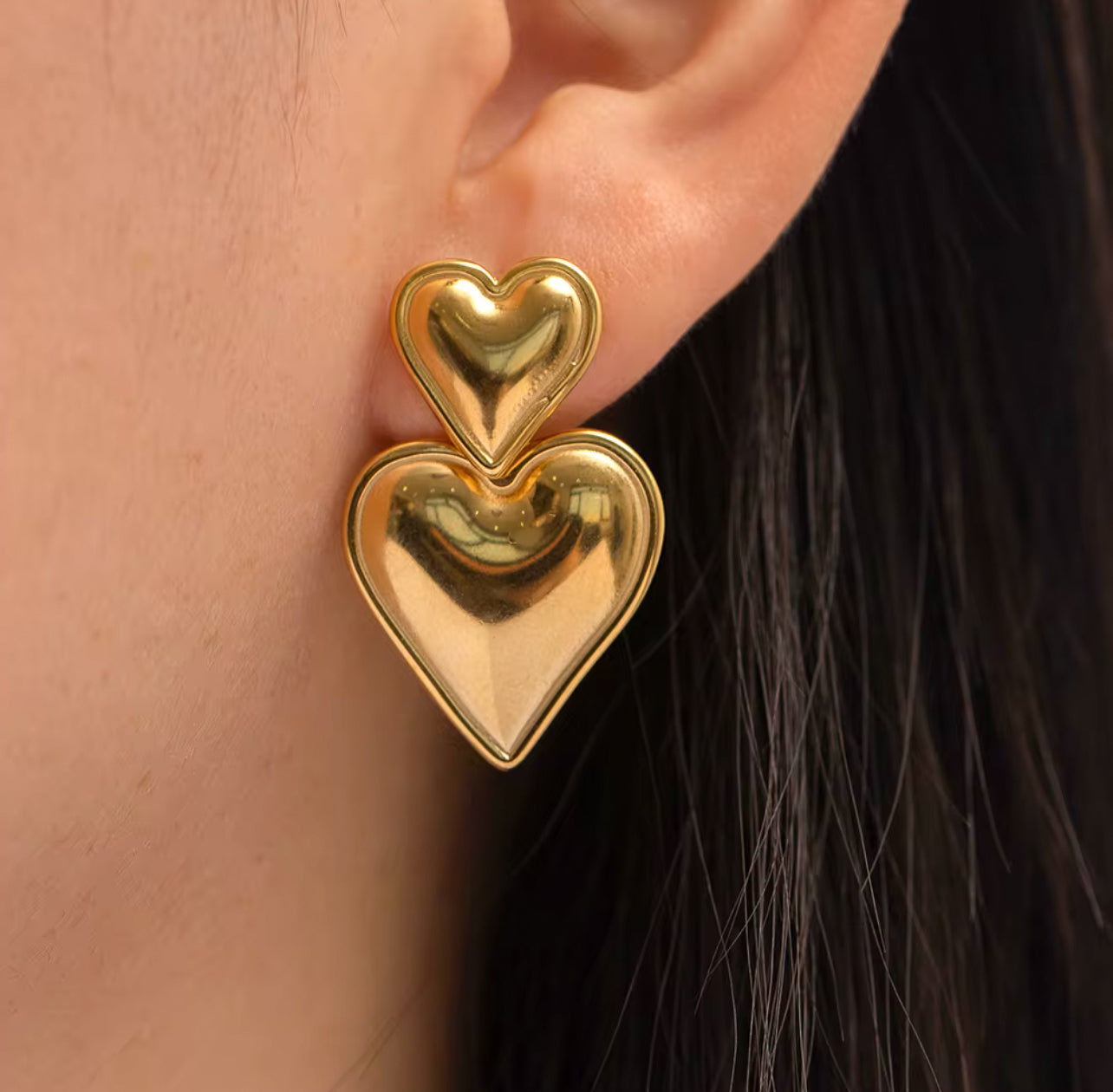 Gold heart-shaped earrings worn by a woman with fair skin and dark hair.