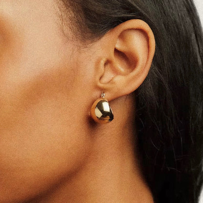 Gold earring worn by a woman with dark skin and dark hair.