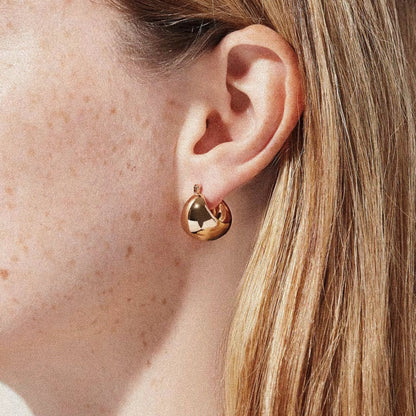 Gold hoop earring worn by a woman with fair skin and blonde hair.