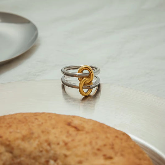 Two interlinked rings, one gold and one silver, on a white surface with a blurred background.