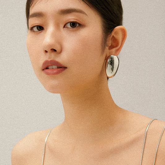 Close-up of a woman wearing silver oval earrings against a neutral background
